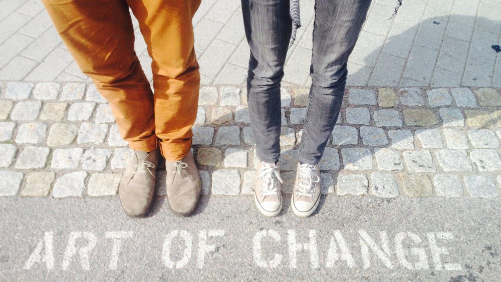 Two people standing on the pavement, before text that says "Art of Change".